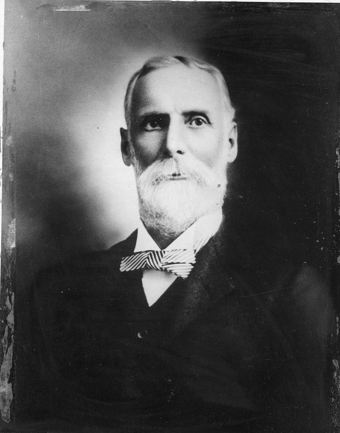A black and white photograph of a person wearing a suit with a bow tie, styled in a manner reminiscent of the early 20th century. 